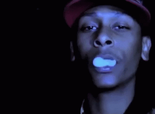 A Man In A Red Hat Is Smoking A Cigarette In The Dark . GIF
