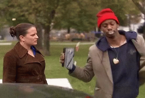 A Man In A Red Hat Is Smoking A Cigarette While Standing Next To A Woman GIF
