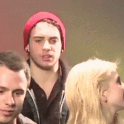 A Man In A Red Hat Is Standing Next To A Woman In A Crowd . GIF