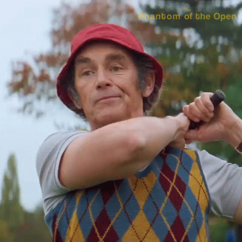 A Man In A Red Hat Is Swinging A Golf Club With The Words Phantom Of The Open Above Him GIF