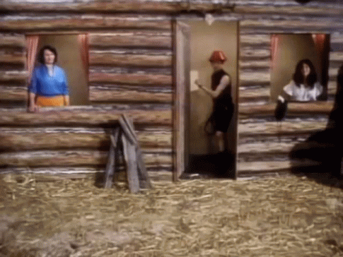 A Man In A Red Hat Stands In A Log Cabin GIF