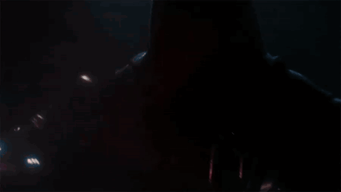 A Man In A Red Helmet Is Holding A Red Light Saber In The Dark . GIF