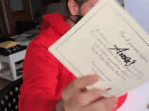 A Man In A Red Hoodie Is Holding A Piece Of Paper With The Name Angel Written On It GIF