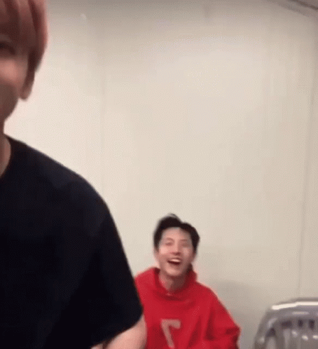 A Man In A Red Hoodie Is Laughing While Another Man In A Black Shirt Looks On . GIF