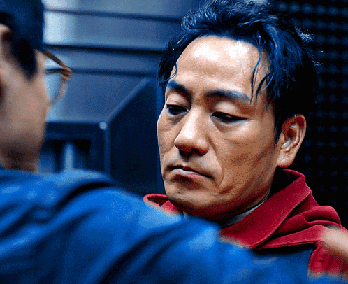 A Man In A Red Hoodie Is Looking At Another Man GIF