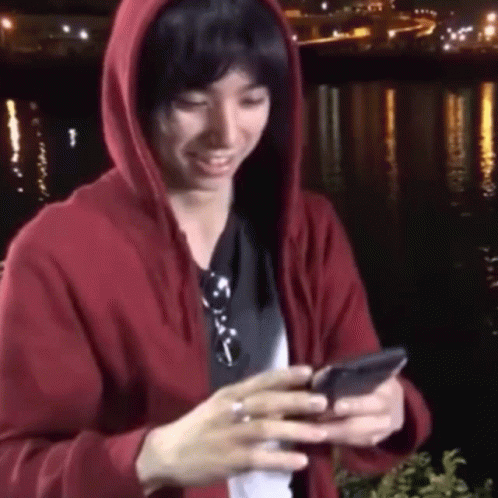 A Man In A Red Hoodie Is Looking At His Cell Phone GIF