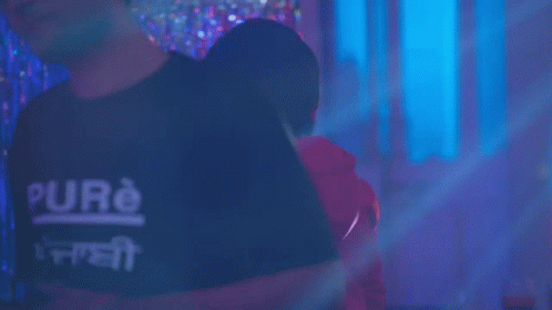 A Man In A Red Hoodie Is Standing In Front Of A Neon Ring GIF