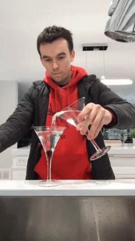 A Man In A Red Hoodie Pours A Martini Into Two Glasses GIF