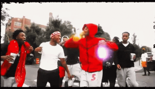A Man In A Red Hoodie With The Letter S On His Shorts Is Surrounded By Other Men GIF