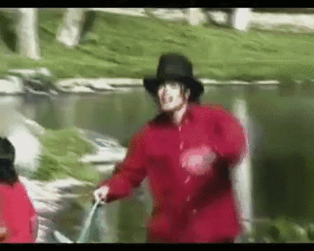 A Man In A Red Jacket And Black Hat Is Walking Across A Grassy Field GIF
