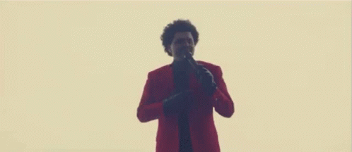 A Man In A Red Jacket And Black Pants Is Standing In Front Of A Wall . GIF