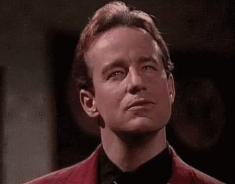 A Man In A Red Jacket And Black Tie Is Making A Face With His Eyes Closed . GIF
