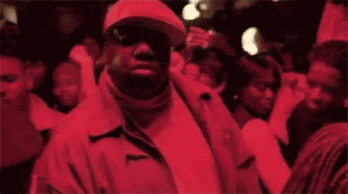 A Man In A Red Jacket And Hat Is Standing In A Crowd Of People GIF