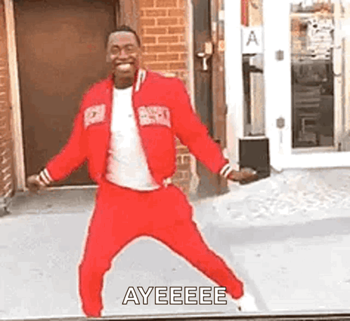 A Man In A Red Jacket And Pants Is Dancing In Front Of A Building . GIF