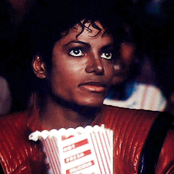 A Man In A Red Jacket Holds A Popcorn Bucket GIF