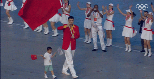 A Man In A Red Jacket Is Carrying A Red Flag And A Boy In A White Shirt Is Holding A Flag GIF