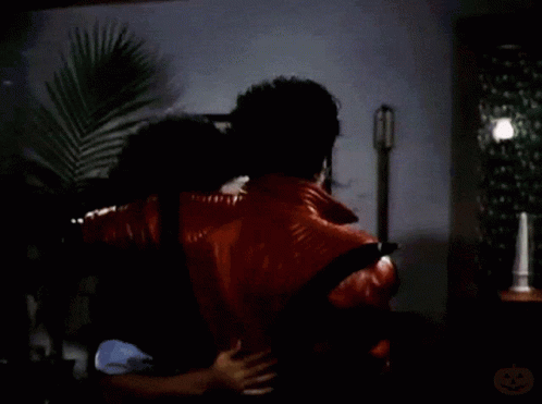 A Man In A Red Jacket Is Carrying Another Man On His Back In A Room GIF