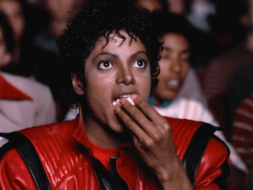 A Man In A Red Jacket Is Eating Popcorn While Watching A Movie GIF