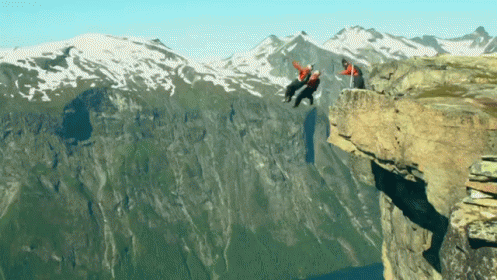 A Man In A Red Jacket Is Hanging Off A Cliff GIF