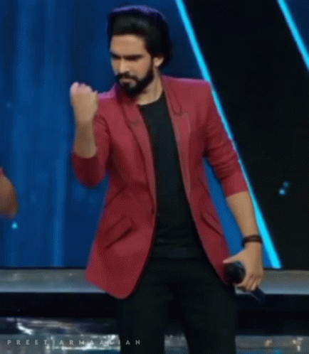A Man In A Red Jacket Is Holding A Microphone And His Fist In The Air GIF