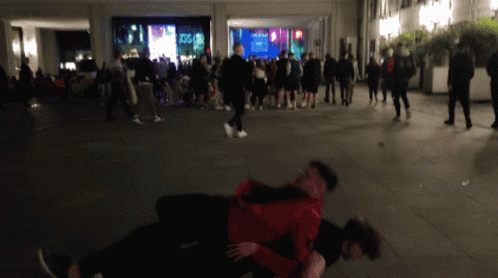 A Man In A Red Jacket Is Holding Another Man In A Crowd GIF