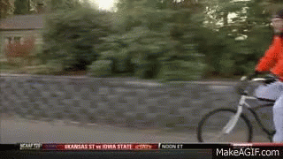 a man in a red jacket is riding a bike down a street with a makeagif.com link in the corner