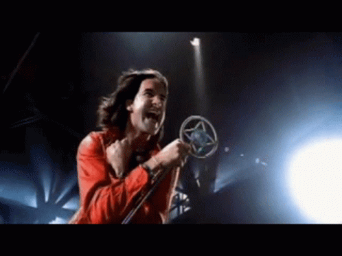 A Man In A Red Jacket Is Singing Into A Microphone On A Stage GIF