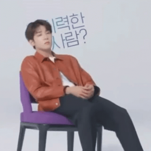 A Man In A Red Jacket Is Sitting In A Chair With His Hands Folded . GIF