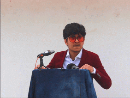 A Man In A Red Jacket Is Standing At A Podium With A Microphone GIF