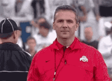 A Man In A Red Jacket Is Standing In A Stadium . GIF