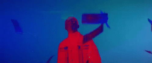 A Man In A Red Jacket Is Standing In Front Of A Blue Background In A Dark Room . GIF