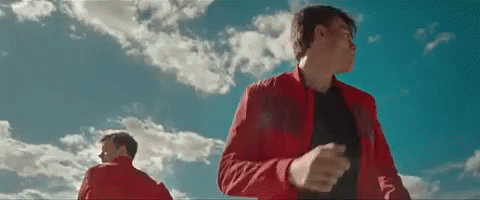 A Man In A Red Jacket Is Standing In Front Of A Blue Sky With Clouds . GIF