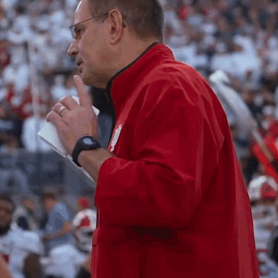 A Man In A Red Jacket Is Standing In Front Of A Crowd Holding A Piece Of Paper GIF