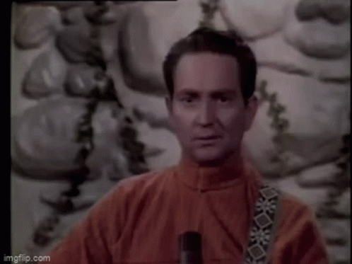 A Man In A Red Jacket Is Standing In Front Of A Painting And Holding A Microphone . GIF
