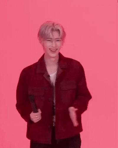 A Man In A Red Jacket Is Standing In Front Of A Pink Background And Clapping . GIF