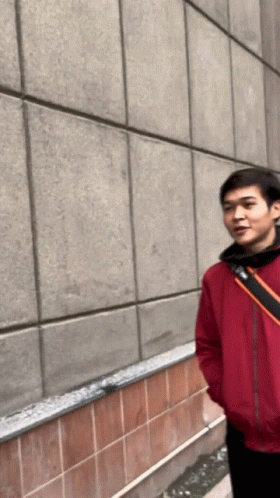 A Man In A Red Jacket Is Standing In Front Of A Tiled Wall GIF