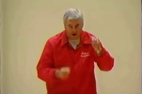A Man In A Red Jacket Is Standing In Front Of A White Wall And Making A Funny Face . GIF