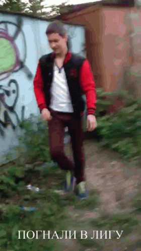 A Man In A Red Jacket Is Walking In Front Of A Wall With Graffiti GIF