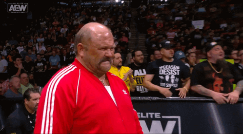 A Man In A Red Jacket Stands In Front Of A Aew Advertisement GIF
