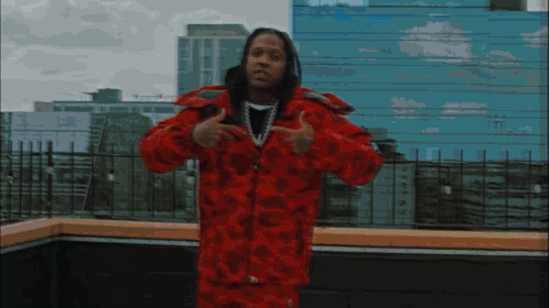 A Man In A Red Jacket Stands In Front Of A Building GIF