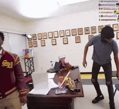 A Man In A Red Jacket With The Letter S On It Stands Next To Another Man GIF