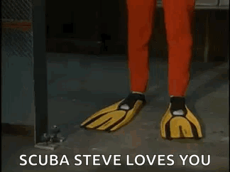 A Man In A Red Jumpsuit And Yellow Gloves Is Standing In A Room And Says `` Scuba Steve Loves You '' GIF