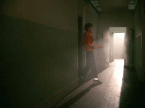A Man In A Red Leather Jacket Is Standing In A Hallway GIF