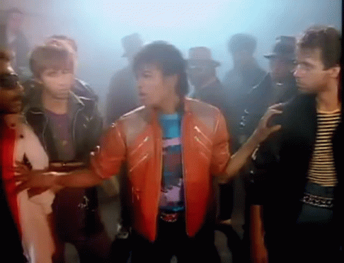 A Man In A Red Leather Jacket Is Standing In Front Of A Crowd Of People . GIF