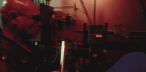 A Man In A Red Mask Is Standing In A Dark Room With A Red Light Behind Him GIF