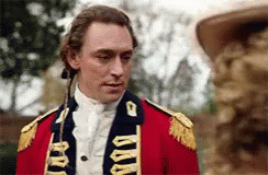 A Man In A Red Military Uniform Is Standing Next To A Statue . GIF