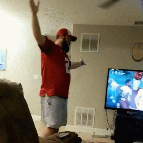 A Man In A Red Number 2 Jersey Stands In Front Of A Tv GIF