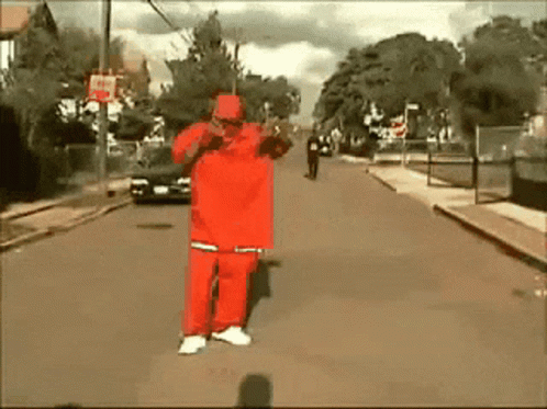A Man In A Red Outfit Is Standing On The Street GIF