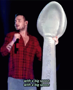 A Man In A Red Plaid Shirt Is Holding A Microphone And A Big Spoon GIF