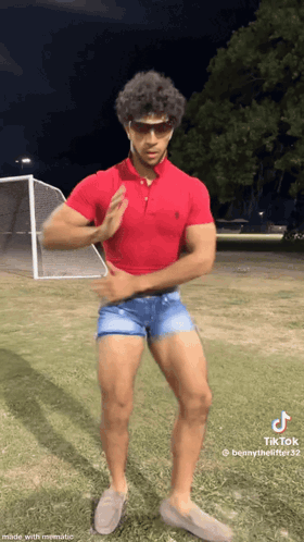 A Man In A Red Polo Shirt And Shorts Is Standing On A Field . GIF